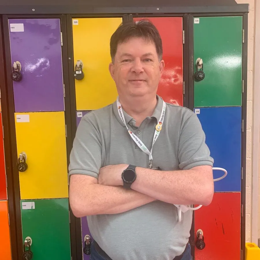Eamonn McKenna, smiling with arms folded in front of a wall of brightly coloured lockers, wearing a grey polo shirt and a CoderDojo Gorey lanyard.